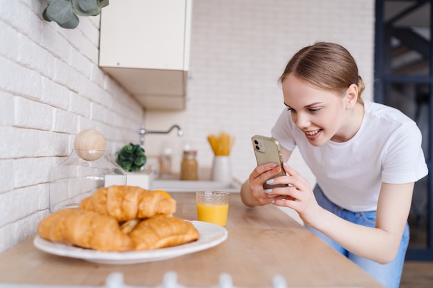 Jonge mooie vrouw die foto op mobiele telefoon van croissants neemt