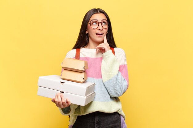 Jonge mooie vrouw die gelukkig glimlacht en dagdroomt of twijfelt, kijkend naar de kant. neem een snel voedselconcept