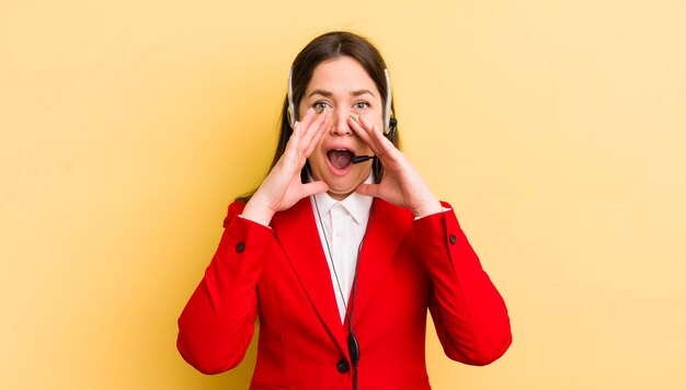 Jonge mooie vrouw die gelukkig voelt en een grote schreeuw geeft met de handen naast het concept van de telemarketeer van de mond