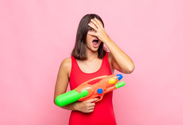 Jonge mooie vrouw die geschokt, bang of doodsbang kijkt, gezicht bedekt met hand en tussen vingers gluurt. zomer concept