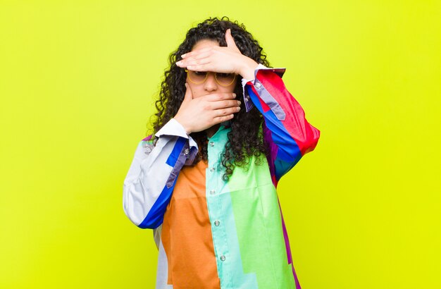 Jonge mooie vrouw die gezicht behandelt met beide handen die nee tegen de camera zegt! het weigeren van afbeeldingen of het verbieden van foto's over een chroma key wall