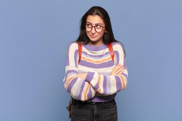 Jonge mooie vrouw die haar schouders ophaalt, zich verward en onzeker voelt, twijfelend met gekruiste armen en een verbaasde blik. studentenconcept