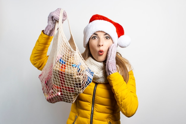 Jonge mooie vrouw die hoed van de Kerstman met geïsoleerde boodschappentassen draagt