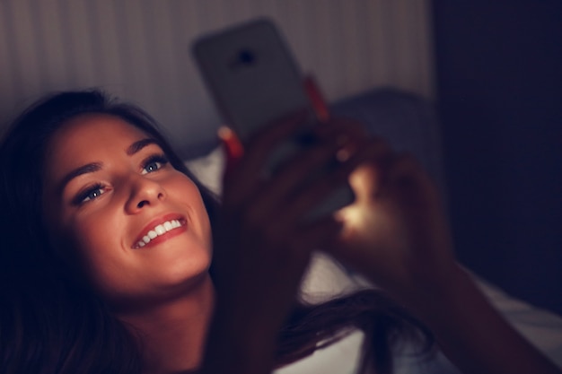 jonge mooie vrouw die in bed met smartphone rust