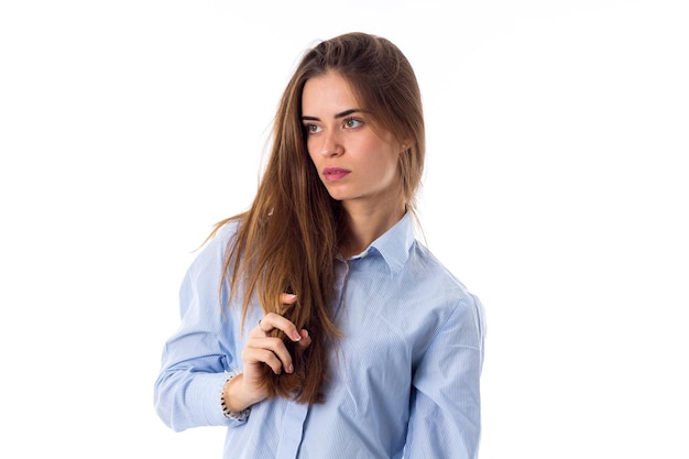 Jonge mooie vrouw die in blauw overhemd haar lang haar op witte achtergrond in studio bevestigt