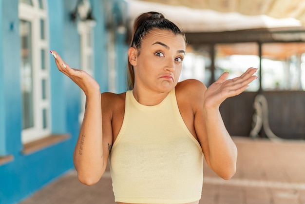 Jonge mooie vrouw die in openlucht twijfelsgebaar maakt