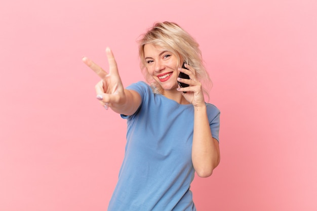 Jonge mooie vrouw die lacht en er gelukkig uitziet, gebarend naar overwinning of vrede