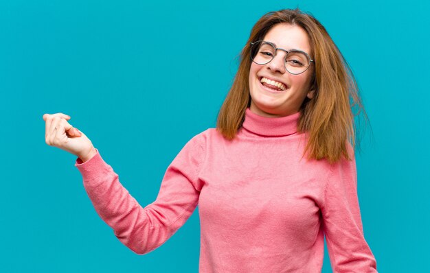 Jonge mooie vrouw die lacht, zorgeloos, ontspannen en gelukkig voelt, danst en naar muziek luistert, plezier maakt op een feestje over de blauwe muur