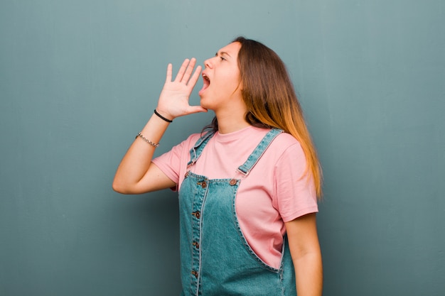 Jonge mooie vrouw die luid en boos schreeuwt om ruimte aan de kant te kopiëren, met hand naast mond over grungemuur