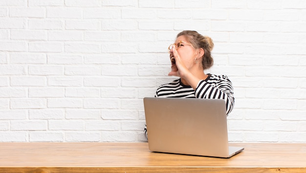 Jonge mooie vrouw die luid en boos schreeuwt om ruimte aan de kant te kopiëren, met hand naast mondzitting met haar laptop