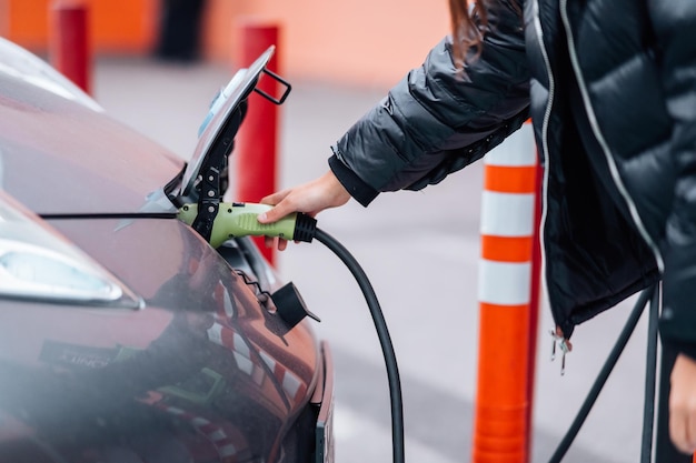 Jonge mooie vrouw die met een elektrische auto reist en stopt bij het laadstation