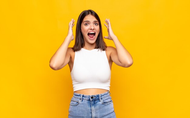 Jonge mooie vrouw die met handen in de lucht schreeuwt, woedend, gefrustreerd, gestrest en boos voelt