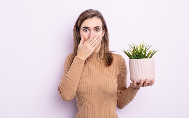 Jonge mooie vrouw die mond bedekt met handen met een geschokt. plant concept