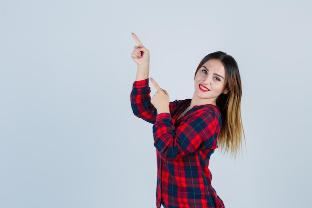 Jonge mooie vrouw die naar de linkerbovenhoek wijst in een casual shirt en er blij uitziet. vooraanzicht.