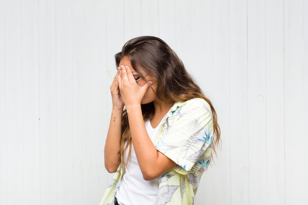 Jonge mooie vrouw die ogen bedekt met handen met een droevige, gefrustreerde blik van wanhoop, huilend, zijaanzicht