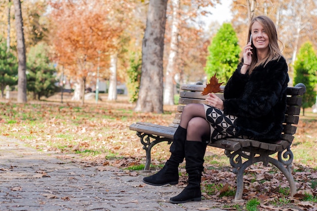 Jonge mooie vrouw die op bank in park zit