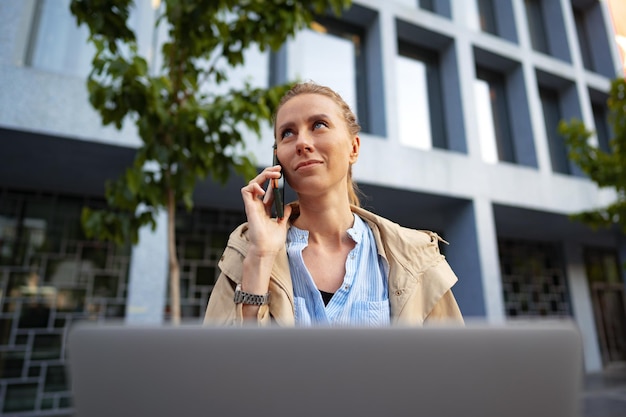 Jonge mooie vrouw die op een laptop werkt die op de bank op straat zit