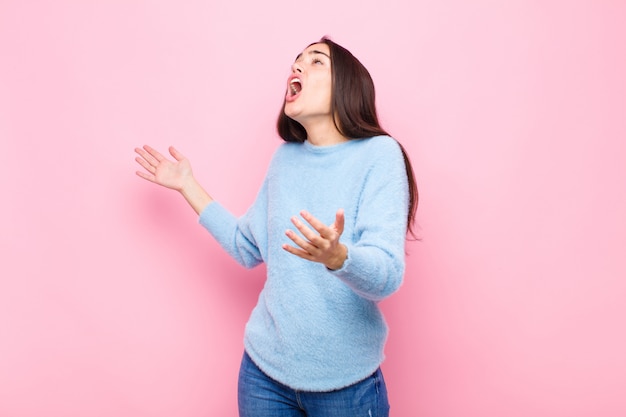 Jonge mooie vrouw die opera uitvoert of bij een concert of show zingt, die romantisch, artistiek en hartstochtelijk voelt tegen roze muur