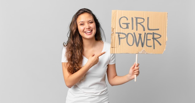 jonge mooie vrouw die opgewonden en verrast kijkt en naar de zijkant wijst en een girl power-banner vasthoudt