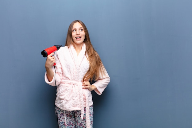 Jonge mooie vrouw die pyjama's draagt en een kapper houdt tegen blauwe muur met een exemplaarruimte