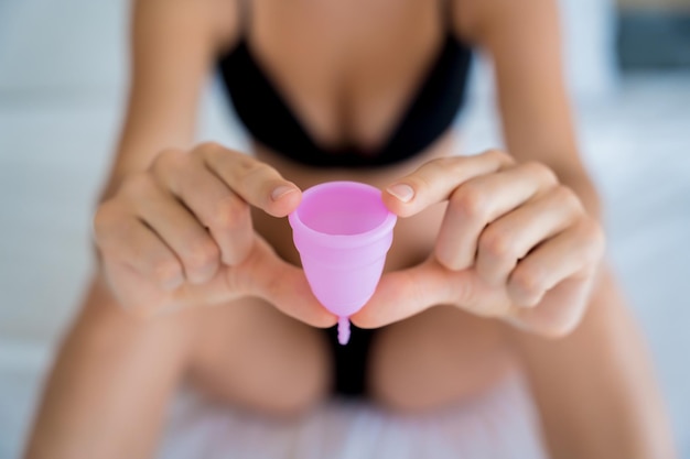 Jonge mooie vrouw die thuis een menstruatiecup in haar handen houdt