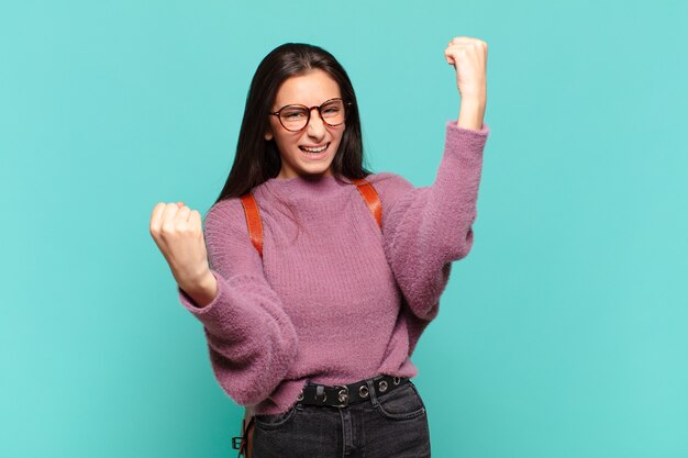 Jonge mooie vrouw die triomfantelijk schreeuwt, eruit ziet als opgewonden, blij en verrast winnaar, viert