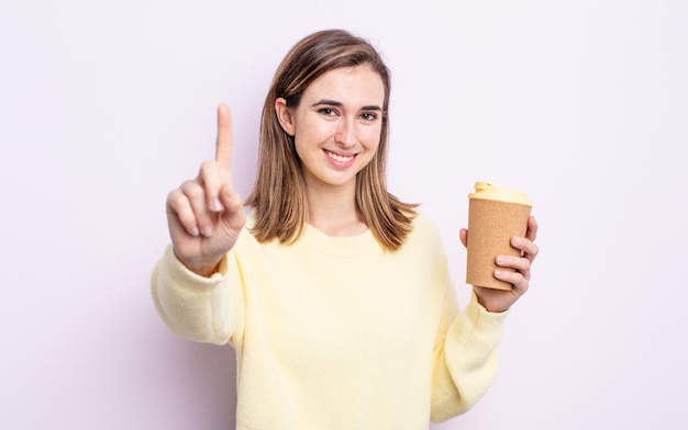 Jonge mooie vrouw die trots en vol vertrouwen glimlacht en nummer één maakt. afhaal koffie concept