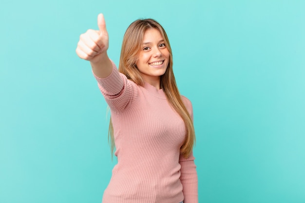 Jonge mooie vrouw die trots is, positief glimlacht met duimen omhoog