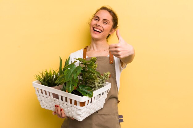 Jonge mooie vrouw die trots positief glimlacht met duimen omhoog plantenconcept