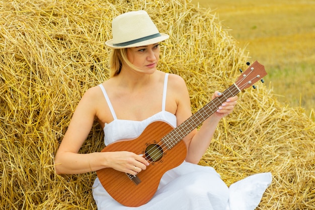 Jonge mooie vrouw die ukelele in hooiberg speelt