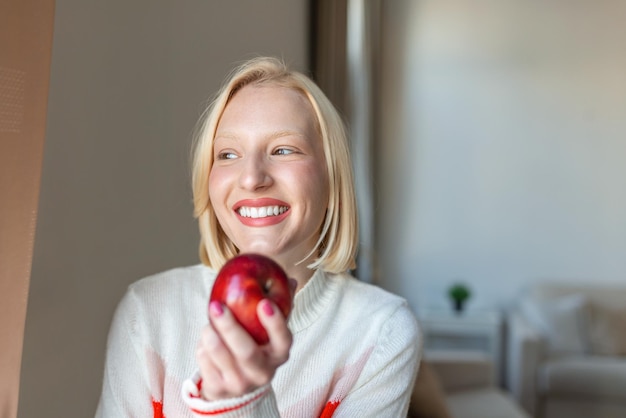 Jonge mooie vrouw die verse appel eet en door venster kijkt