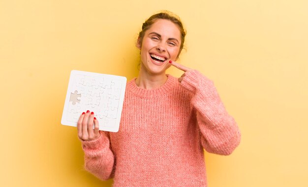 Jonge mooie vrouw die vol vertrouwen glimlacht en wijst naar het eigen brede glimlachpuzzelconcept