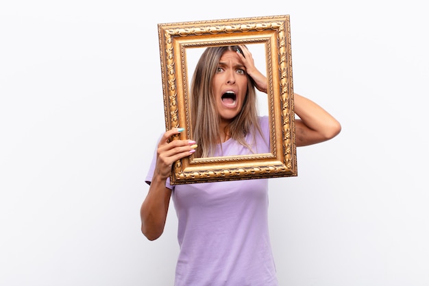 Jonge mooie vrouw die walging en geïrriteerd voelt, tong uitsteekt, niet van iets smerigs en vies houdt met een barok frame.