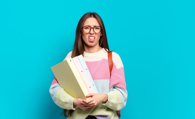 Jonge mooie vrouw die walgt en geïrriteerd voelt, tong uitsteekt, niet van iets smerigs en vies houdt