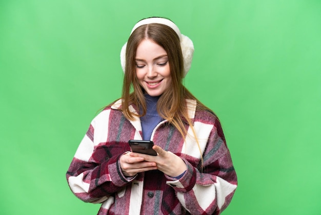 Jonge mooie vrouw die wintermoffen draagt over geïsoleerde chroma key-achtergrond die een bericht verzendt met de mobiel