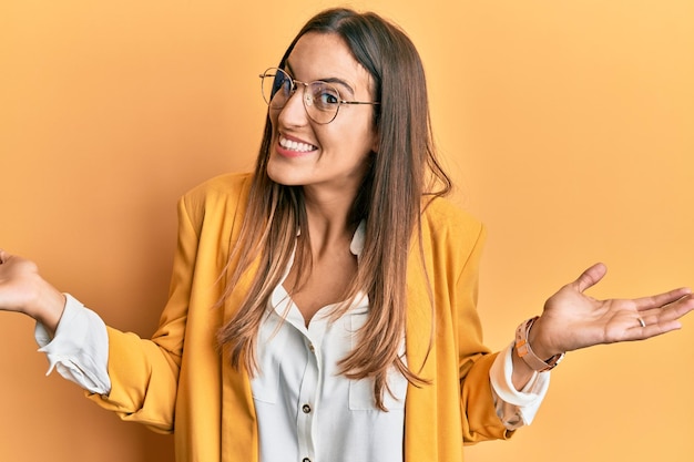 Jonge mooie vrouw die zakelijke stijl en bril draagt die glimlacht en beide handen open handpalmen laat zien en reclame maakt voor vergelijking en balans