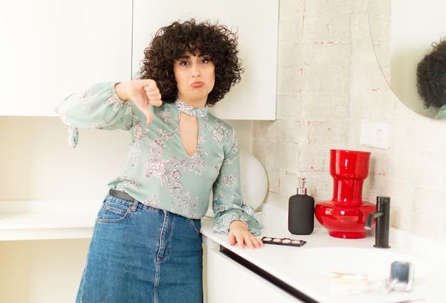 Jonge mooie vrouw die zich boos, boos, geïrriteerd, teleurgesteld of ontevreden voelt, duimen naar beneden laat zien met een serieuze blik