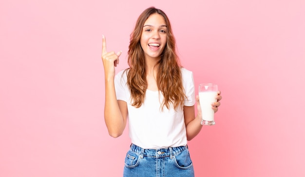 Jonge mooie vrouw die zich een gelukkig en opgewonden genie voelt nadat ze een idee heeft gerealiseerd en een glas melk vasthoudt