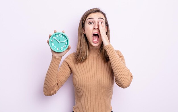 Jonge mooie vrouw die zich gelukkig voelt, een grote schreeuw geeft met de handen naast de mond. wekker