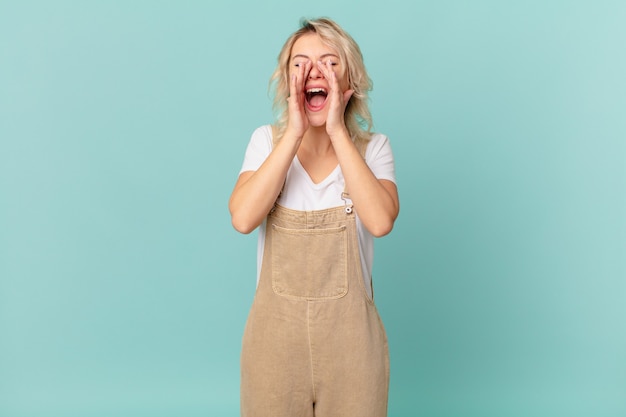 Jonge mooie vrouw die zich gelukkig voelt, een grote schreeuw geeft met de handen naast de mond