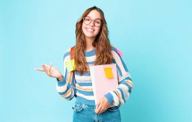 Jonge mooie vrouw die zich gelukkig voelt, verrast een oplossing of idee realiseert met een tas en boeken vasthoudt