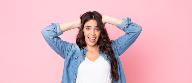 Jonge mooie vrouw die zich gestrest, bezorgd, angstig of bang voelt, met de handen op het hoofd, in paniek bij vergissing