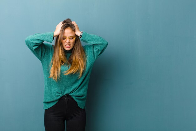 Jonge mooie vrouw die zich gestrest en gefrustreerd voelt, handen opheft, zich moe, ongelukkig en met migraine voelt