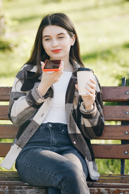 Jonge mooie vrouw die zich op een bank bevindt die de telefoon met behulp van