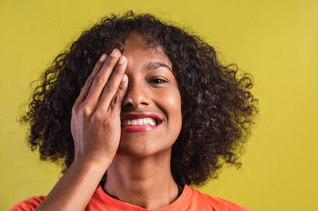 Jonge mooie vrouw die zich op gele geïsoleerde achtergrond bevindt die één oog met hand behandelt.