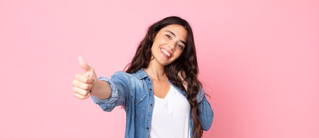 Jonge mooie vrouw die zich trots, zorgeloos, zelfverzekerd en gelukkig voelt, positief glimlachend met duimen omhoog