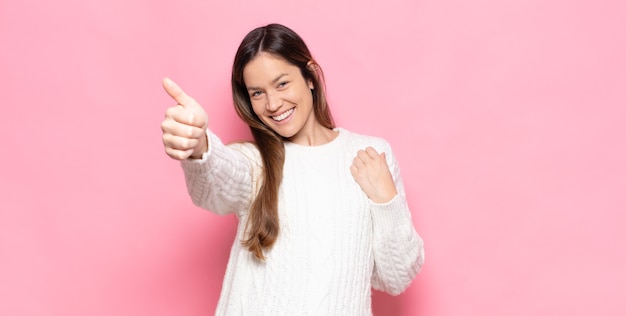 Jonge mooie vrouw die zich trots, zorgeloos, zelfverzekerd en gelukkig voelt, positief glimlacht met omhoog duimen