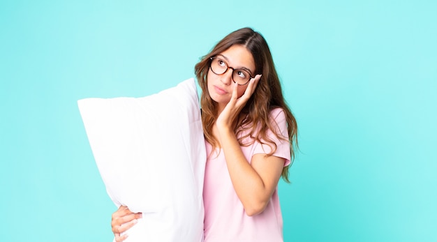 jonge mooie vrouw die zich verveeld, gefrustreerd en slaperig voelt na een vermoeiende pyjama te dragen en een kussen vast te houden