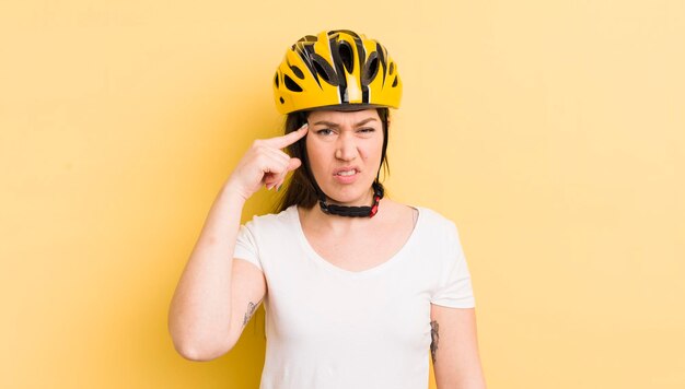 Jonge mooie vrouw die zich verward en verbaasd voelt en laat zien dat je een krankzinnig fietshelmconcept bent