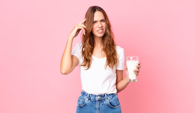 jonge mooie vrouw die zich verward en verbaasd voelt, laat zien dat je gek bent en een glas melk vasthoudt